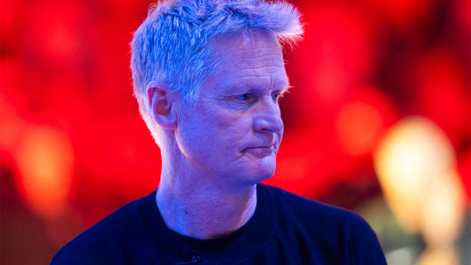 Steve Kerr in close-up, looking to the side against a red, blurred background
